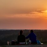 deux personnes assises sur une colline regardant le coucher du soleil