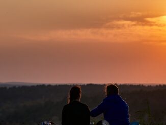 deux personnes assises sur une colline regardant le coucher du soleil