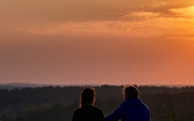 deux personnes assises sur une colline regardant le coucher du soleil