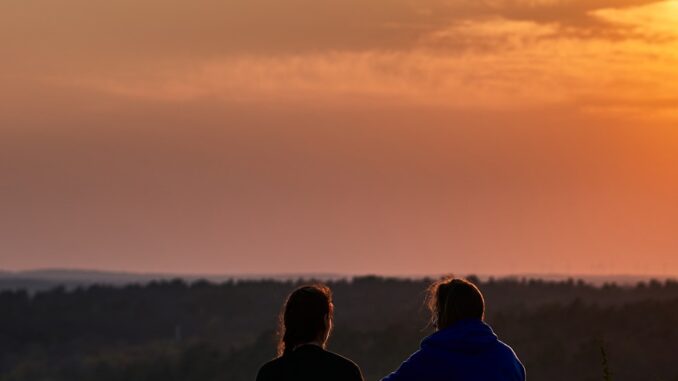 Week-end en amoureux deux personnes assises sur une colline regardant le coucher du soleil